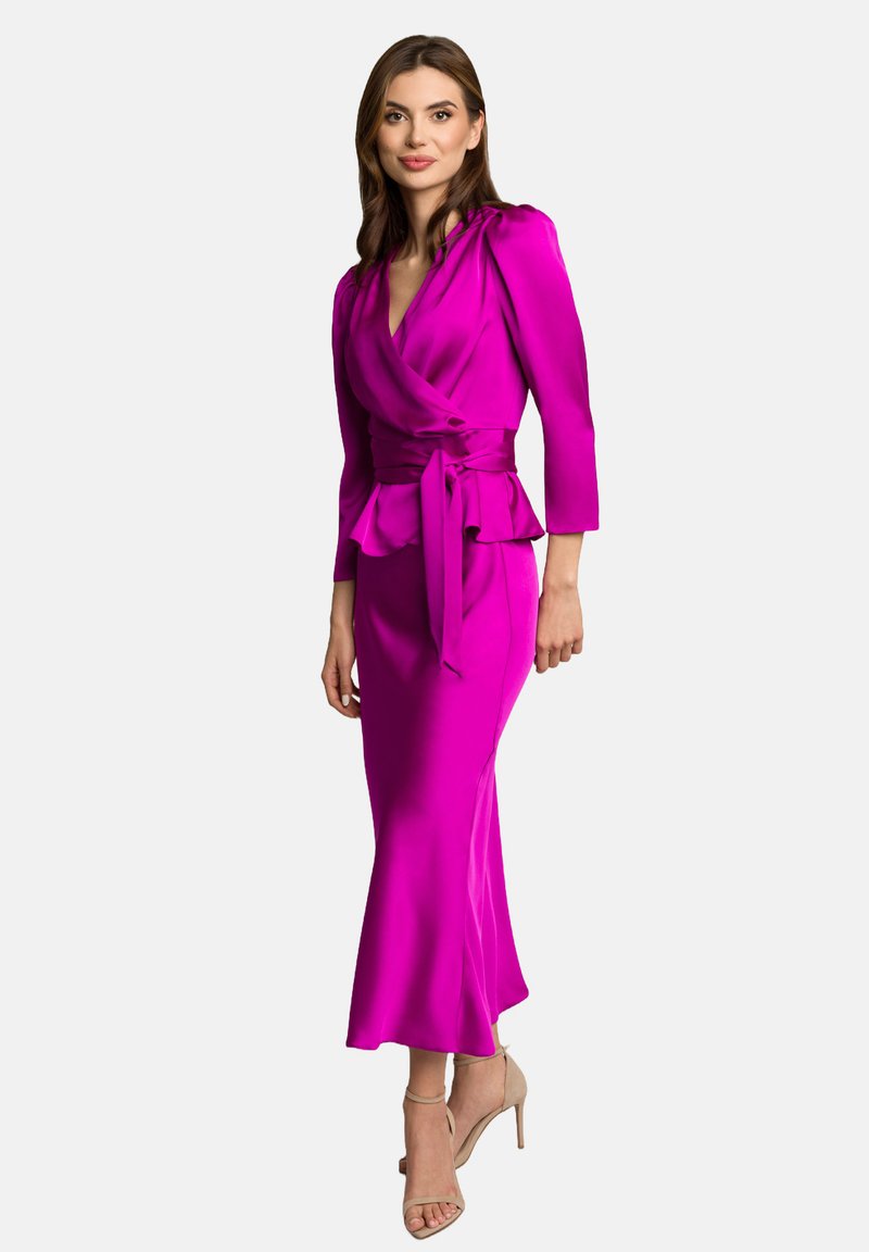 Fuksjowa satynowa sukienka z konstrukcją w stylu wrap, 3/4 rękawami, peplum w talii i długością do ziemi. Połączona z cielistymi sandałami na wysokim obcasie.