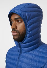 Chaqueta acolchada azul con capucha, que presenta un diseño acolchado, textura suave, cierre de cremallera completa y forro interior en un color contrastante.