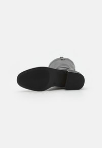 Bottine en cuir gris avec une semelle en caoutchouc noir texturé. Présente une finition lisse et une petite sangle décorative à l'arrière.