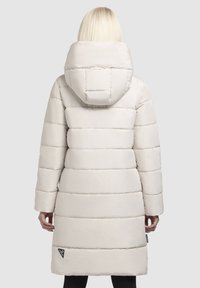 Manteau matelassé blanc avec une grande capuche, présentant des lignes de couture horizontales, des manches longues et une étiquette logo sur le côté, près de l'ourlet inférieur.