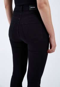 Vaqueros ajustados de talle alto de denim negro con bolsillos traseros y una etiqueta de marca en la cinturilla, que presentan una textura suave y mate.