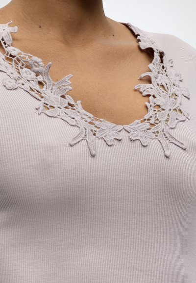 Κοντινό πλάνο ροζ ριμπ μπλουζάκι με V-λαιμόκοψη και διακοσμητική δαντέλα με λουλούδια γύρω από την περιοχή των κλείδων.