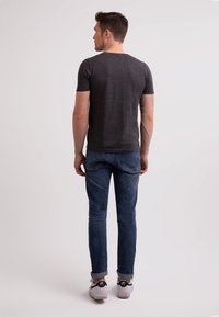 Tmavě šedé tri�čko s krátkým rukávem v kombinaci s modrými slim-fit džíny a bílými teniskami, pohled zezadu na neutrálním pozadí.