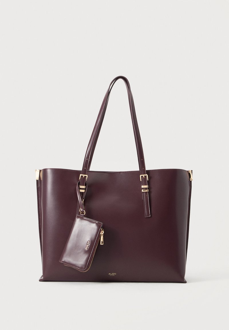 Sac cabas en cuir marron foncé avec deux anses épaules et une pochette zippée assortie fixée, sur un fond clair uni.
