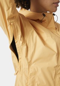 Chaqueta impermeable amarilla con un alto cuello, cordón ajustable y ventilaciones laterales con cremallera. Textura suave y diseño ligero.