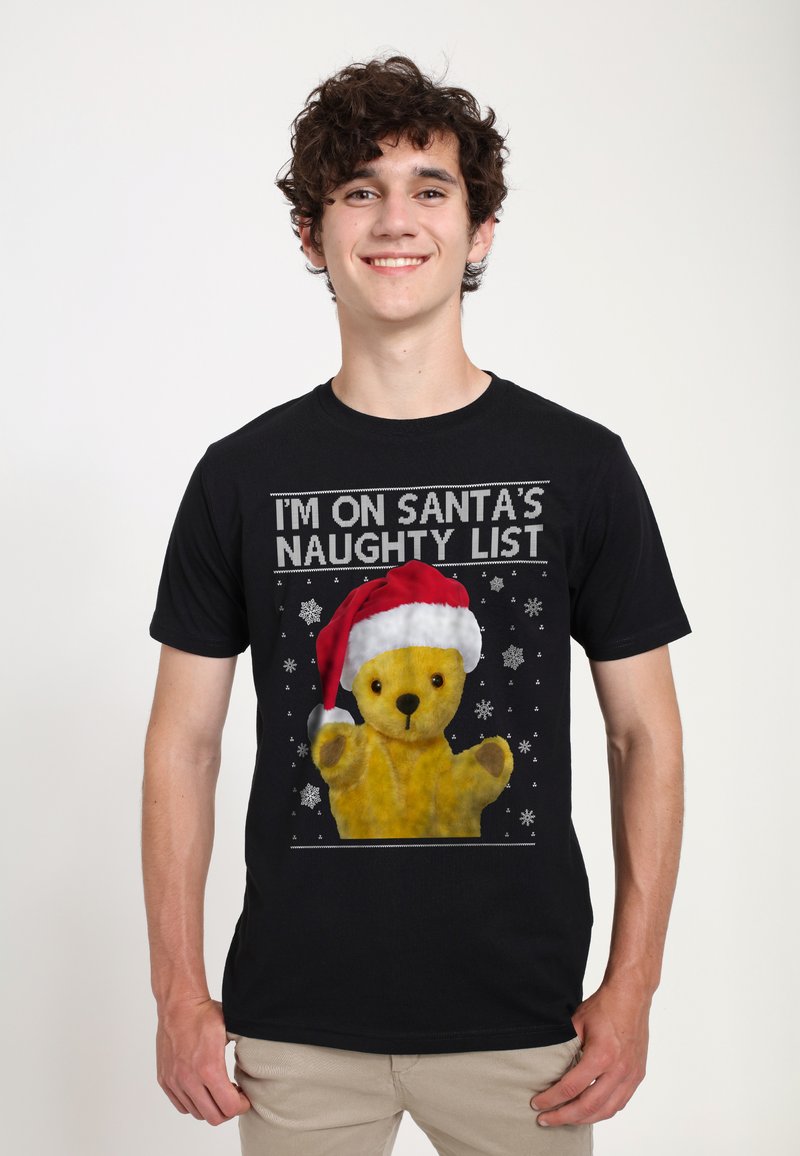 Zwarte T-shirt met een afbeelding van een gele teddybeer in een rode kerstmanhoed, met tekst "IK STA OP SANTA'S SLECHTE LIJST" en sneeuwvlokken.