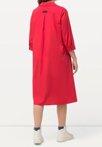 Punainen nappikaulusmekko, jossa on kolme neljännesosa hihaa, löysä malli ja takapanelin yksityiskohta. Yhdistetty valkoisiin nilkkureihin, joissa on sinisiä yksityiskohtia.