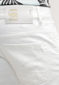 Jean en denim blanc avec une étiquette logo G-Star RAW sur la ceinture. Comprend des poches arrière avec des détails de couture subtils.