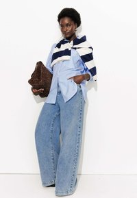 Chemise bleue à rayures avec des boutons, jeans oversize bleu clair, écharpe rayée bleu marine et blanche, et pochette en imprimé léopard marron.