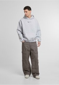 Sudadera gris de gran tamaño con cordón y bolsillo frontal, combinada con pantalones cargo sueltos de color caqui que cuentan con múltiples bolsillos y un ajuste relajado.