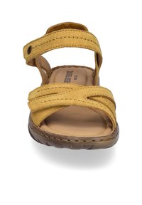 Sandale en suède jaune avec des brides croisées, une semelle intérieure rembourrée et une semelle en caoutchouc flexible. Dotée d'une fermeture à boucle et crochet pour un ajustement facile.