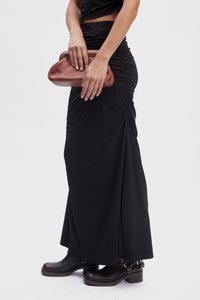 Svart, rynket maxi skjørt med en glatt tekstur, kombinert med en brun, myk clutch-veske. Svart hæl ankler støvler med spennel detaljer.