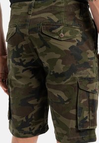Pantalones cortos de camuflaje en verde y marrón. Fabricados con un tejido duradero, cuentan con bolsillos laterales y solapas en la parte trasera. La marca es visible en la pierna.