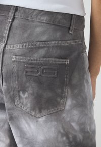 Falmet grå denimjeans med en lappelomme med preget logo-detalj. Stoffet har en lett glans med kontrasterende sømmer.