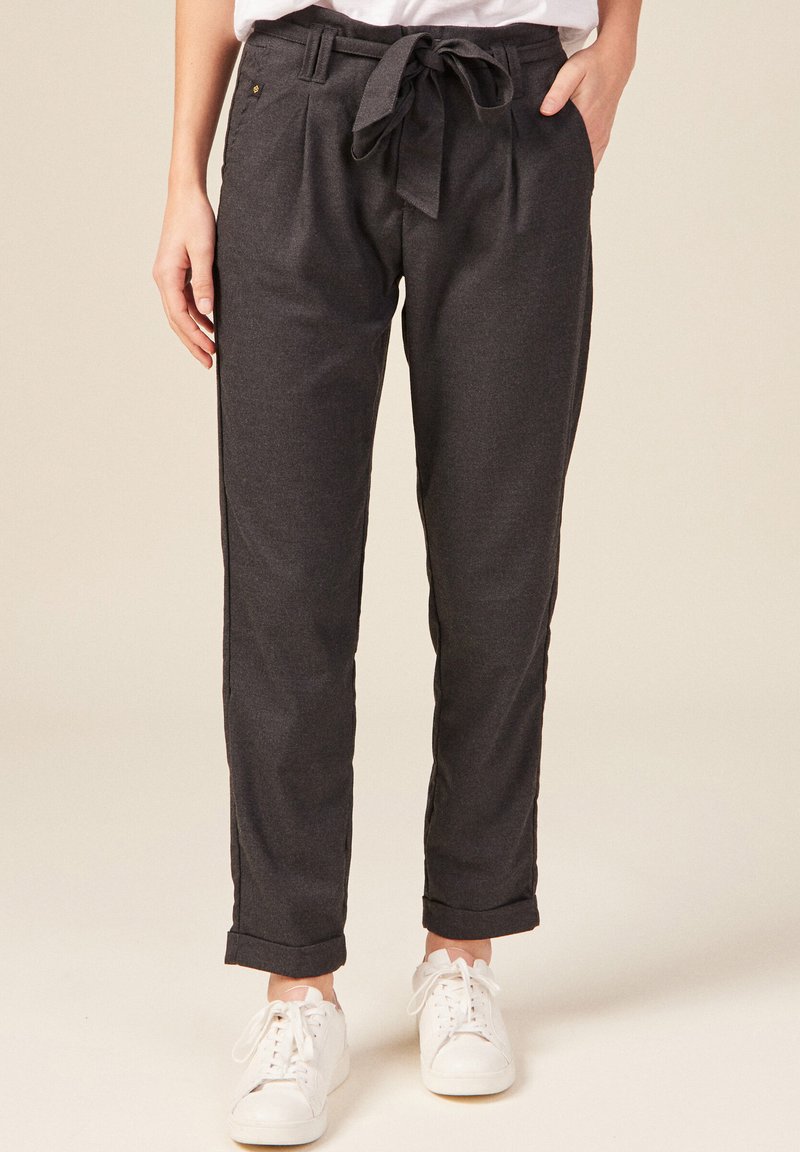 Kolsvart byxor med bälte i midjan, framfållar, snedställda fickor och uppvikta fållar, i kombination med vita sneakers.