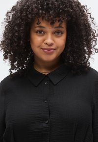 Μαύρο πουκάμισο με γιακά και κουμπιά στο μπροστινό μέρος, υφασμένο ύφασμα με υφή, διακριτική λάμψη, που διαθέτει κλασικό σχέδιο και ομαλές λεπτομέρειες γιακά.