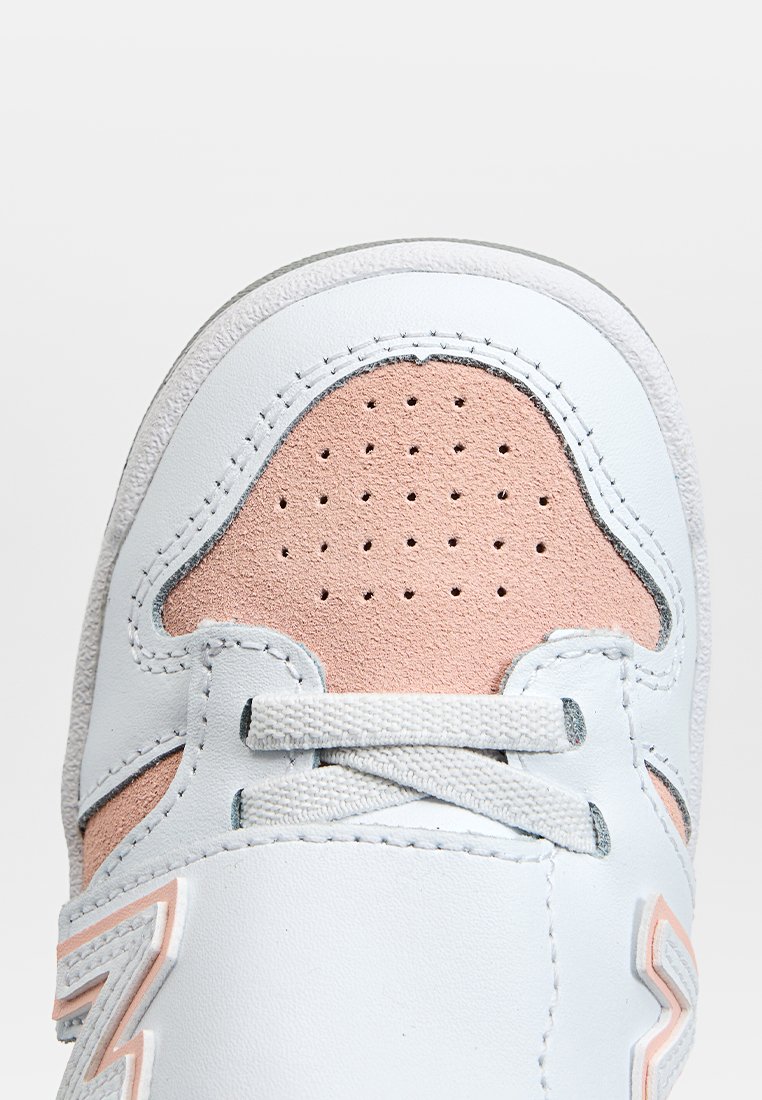 Scarpa atletica in pelle con un corpo bianco, dettagli in suede rosa, punta perforata e cuciture grigie. Presenta lacci piatti e una suola testurizzata.