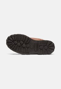 Bota de cuero marrón con una suela de goma negra resistente, que presenta surcos profundos y una superficie texturizada para mayor tracción. Cuerdas y costuras reforzadas visibles.