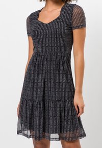 Schwarzes Kleid mit kurzen transparenten Ärmeln, V-Ausschnitt, strukturierten vertikalen Streifen und einem ausgestellten, gestuften Rock. Insgesamt leichter Stoff mit dezenten Mustern.