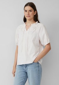 Jasnoróżowa bluzka w paski z dekoltem w kształcie litery V i marszczonym wykończeniem, krótkimi bufiastymi rękawami oraz luźnym krojem. Wykonana z miękkiego, lekkiego materiału.