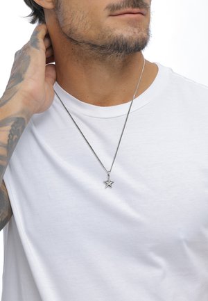 Silver star pendant necklace with a textured design, hanging from a thin metal chain, worn over a plain white t-shirt.