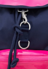 Fermoir métallique fixé à un tissu bleu marine avec des nœuds en cordon noir et une fermeture éclair rose avec une bordure en dessous.