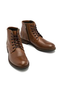 Brązowe skórzane botki za kostkę o gładkiej fakturze, z wiązaniem z przodu i zamkiem błyskawicznym z boku. Wyróżniają się okrągłym noskiem i płaską podeszwą dla stabilności.