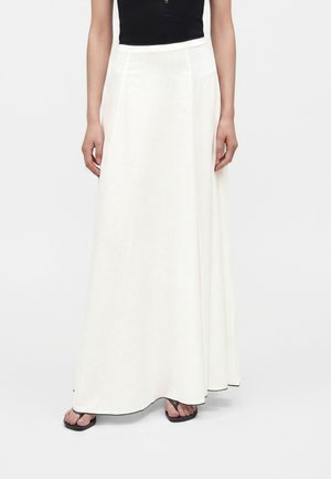 Femme portant une longue jupe blanche fluide avec un bord noir, associée à un haut noir sans manches et des sandales noires.