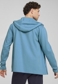 Lysblå hættetrøje med tekstureret stof, lange ærmer og snor til hætten. Har sideskår og et afslappet fit design.