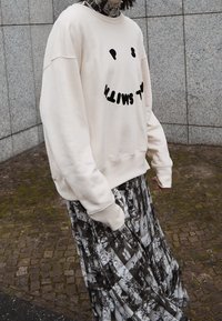 Krémový oversized svetr s černým textem, doplněný dlouhou sukní s černobílým vzorem. Příjemný materiál s kleslými rameny.