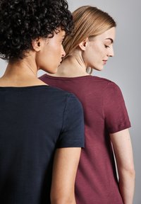 Due magliette esposte di spalle: una blu navy, a maniche corte; l'altra borgogna, a maniche corte. Entrambe presentano un collo rotondo e una consistenza morbida.