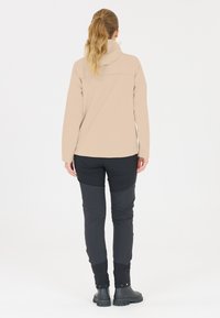 Beige långärmad topp med hög krage, i kombination med åtsittande svarta byxor. Byxorna har kontrasterande paneler och svarta stövlar med strukturerad sula.