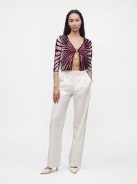 Femme portant un pantalon blanc taille haute à jambes larges, des talons pointus et un cardigan court à motifs noirs et roses avec un détail anneau à l'avant.