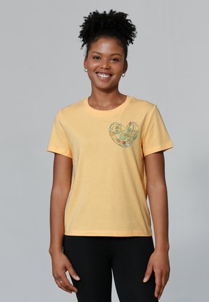 Gelbes Baumwoll-T-Shirt mit kurzen Ärmeln, versehen mit einem grünen Herzgrafik auf der Brust. Glatte Textur, normale Passform.
