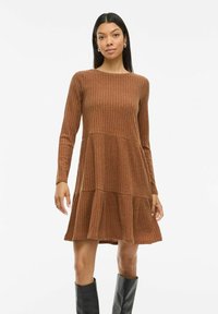 Braunes, geripptes Strickkleid mit langen Ärmeln, rundem Ausschnitt und einem gestuften Rockdesign. Es zeichnet sich durch einen enganliegenden Oberteil und schwingende untere Abschnitte aus.