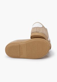 Scarpe slip-on in suede beige con dettagli bianchi, punta tonda e suola in gomma testurizzata. Presentano un design cucito e l'etichetta "Made in Spain".