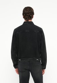 Μαύρο τζιν μπουφάν με κλασικό γιακά, μακριά μανίκια και κουμπωτές μανσέτες. Η πλάτη έχει ομαλή υφή με ελάχιστες ραφές.