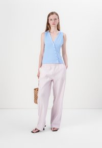Top sin mangas de rayas azul claro con escote en V y cierre de botones, combinado con pantalones de pierna ancha de rayas rosas y blancas y un bolso de mimbre.