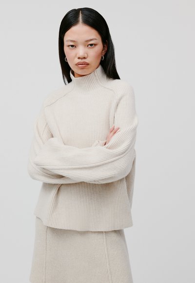 Maglione a coste color crema con collo alto, spalle scese e vestibilità rilassata, caratterizzato da un motivo testurizzato e un tessuto morbido e accogliente.