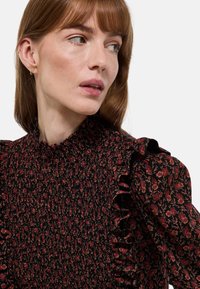 Robe noire avec des motifs floraux rouges et beiges. Comprend un buste froncé et des manches volantées, fabriquée en tissu léger.