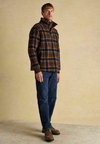 Brown and navy plaid pullover with a high collar, made of textured fleece; paired with blue jeans and brown lace-up boots.