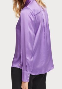 Blusa di seta viola con colletto, maniche lunghe con polsini abbottonati e una vestibilità leggermente morbida con piega sul retro.