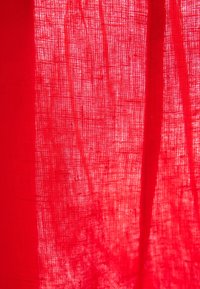 Gros plan d'un tissu translucide rouge vif avec des fibres visibles et la lumière filtrant à travers la texture tissée.
