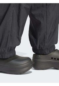 Mustat vedenpitävät housut elastisilla hihansuilla, yhdistettynä tummanharmaisiin puukkoihin, joissa on tuuletusaukoja ja sileä, mattapintainen pinta.