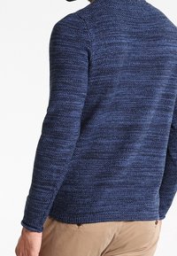 Navy blue knitted crew neck sweater with textured pattern, long sleeves, and ribbed hem. Features a casual, relaxed fit.