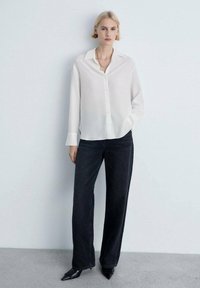 Hvid skjorte med krave, parret med sort vidde jeans og sorte spidse sko. Glat stof med en afslappet pasform.