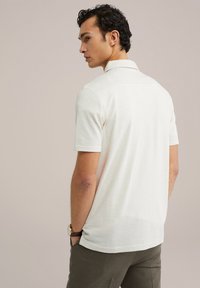 Polokamiza s kratkimi rokavi v off-white teksturiranem materialu, z ovratnikom in slim fit krojem, v kombinaciji z olivno zelenimi hlačami.