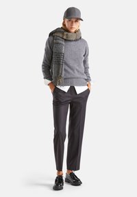 Szary sweter dzianinowy, biały koszulowy podkoszulek, szalik w kratę, ciemne spodni w paski oraz czarne buty z grubą podeszwą. Szara czapka.