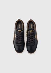 Baskets en daim noir et en cuir avec des accents bruns, des lacets foncés et des détails dorés, arborant un logo « Harry Potter » sur la semelle intérieure.