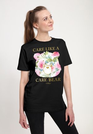 Czarny bawełniany t-shirt z kwiatowym motywem "Care Bear" i złotym tekstem "CARE LIKE A CARE BEAR 1982." Krótkie rękawy i luźny krój.